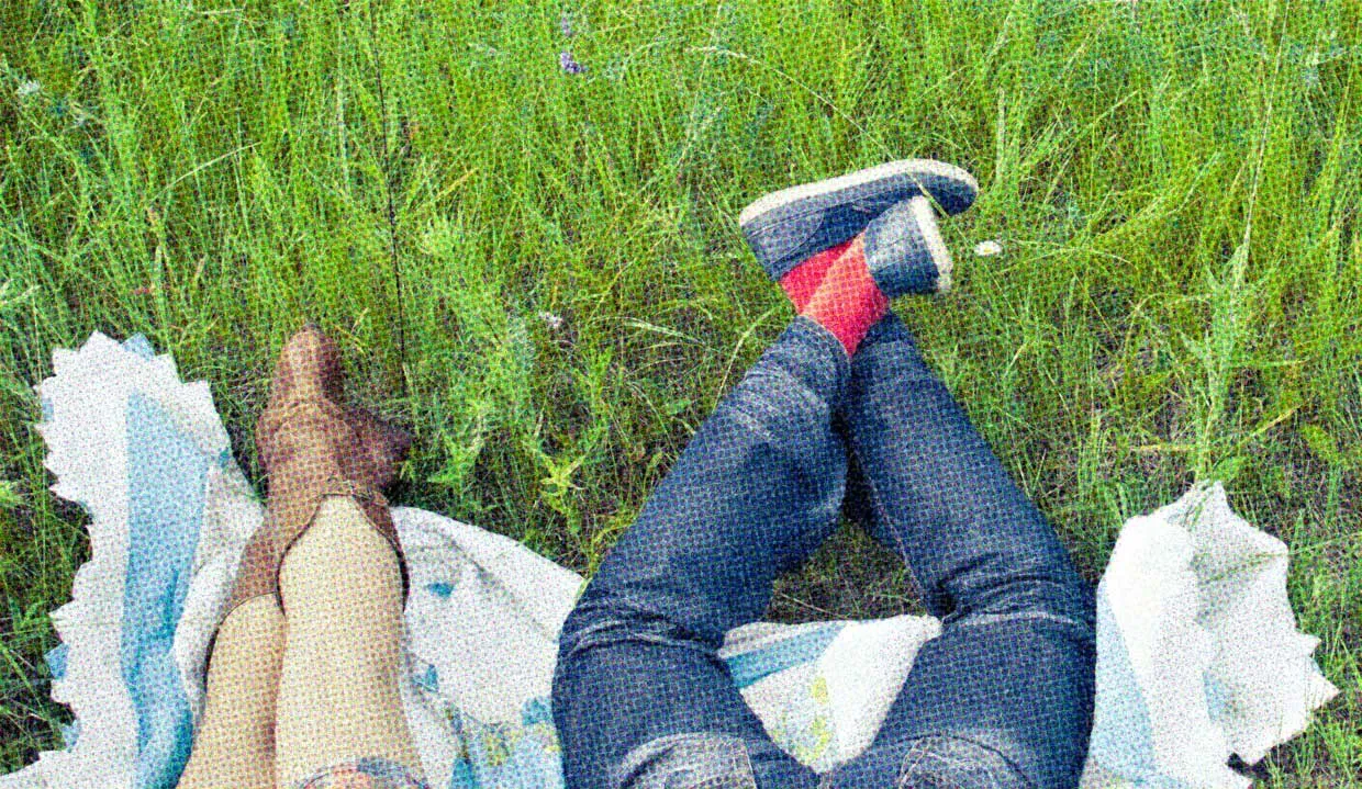 The legs of two people on a picnic blanket on the grass. They're still dressed... But for how long?