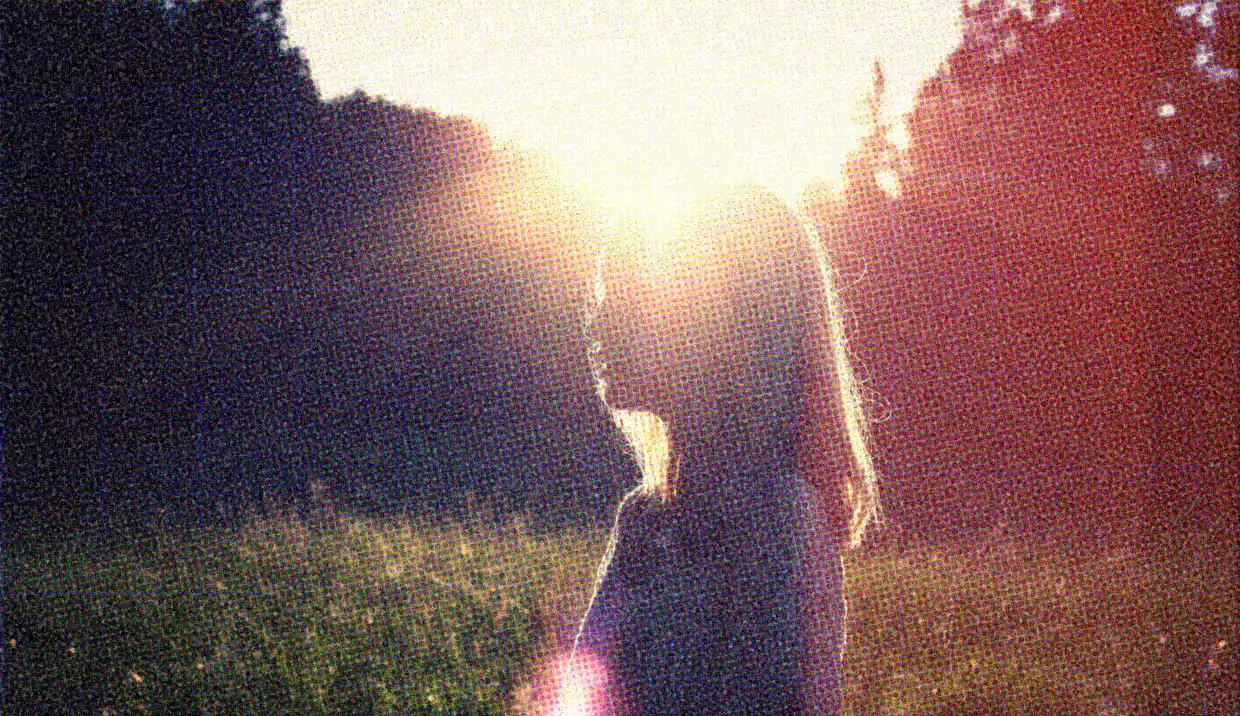 A woman stands outdoors, with the sun shining on her.