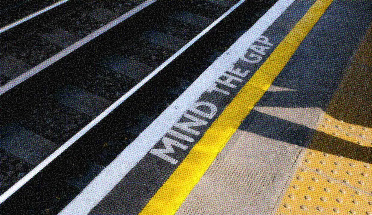 A close-up of a train platform with the words MIND THE GAP stenciled next to the edge.