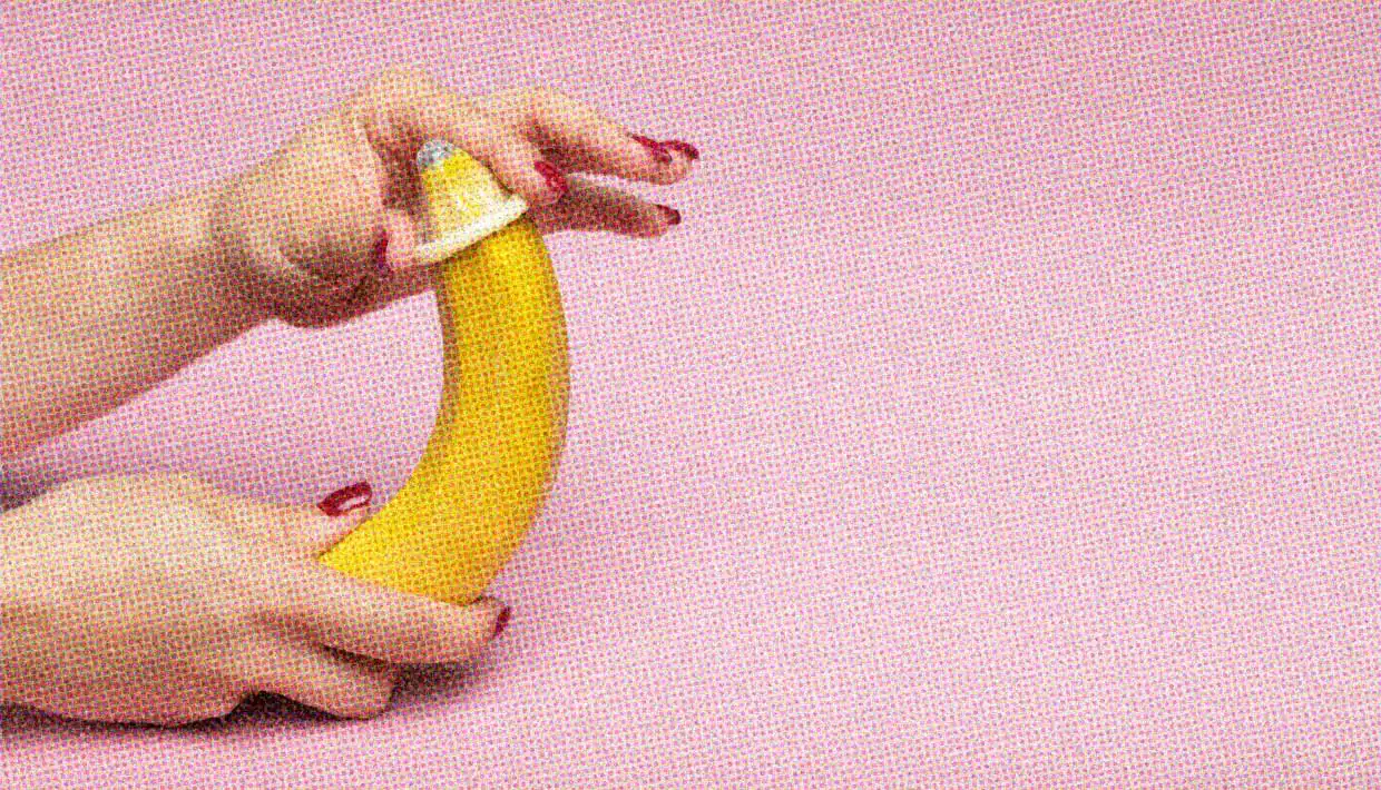 A close-up of a pair of hands putting a condom on a banana.
