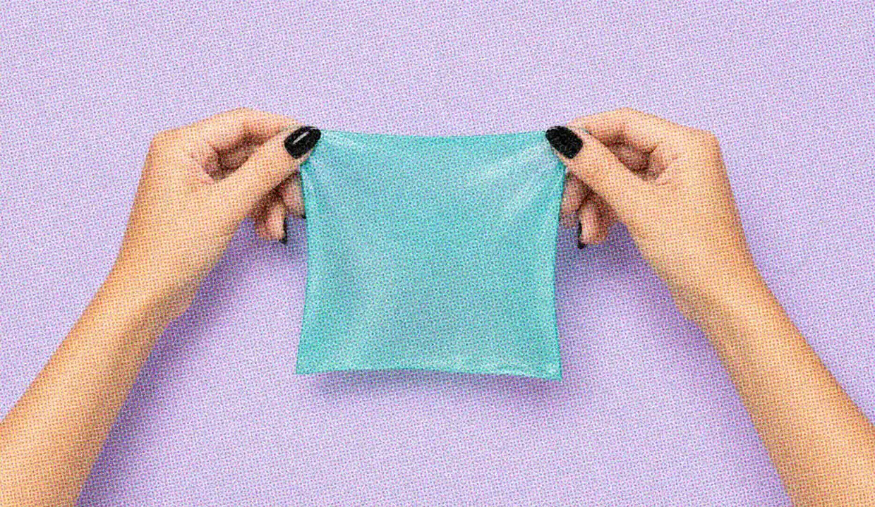 Hands with black nail polish holding a turquoise dental dam stretched out against a pale lavender background.