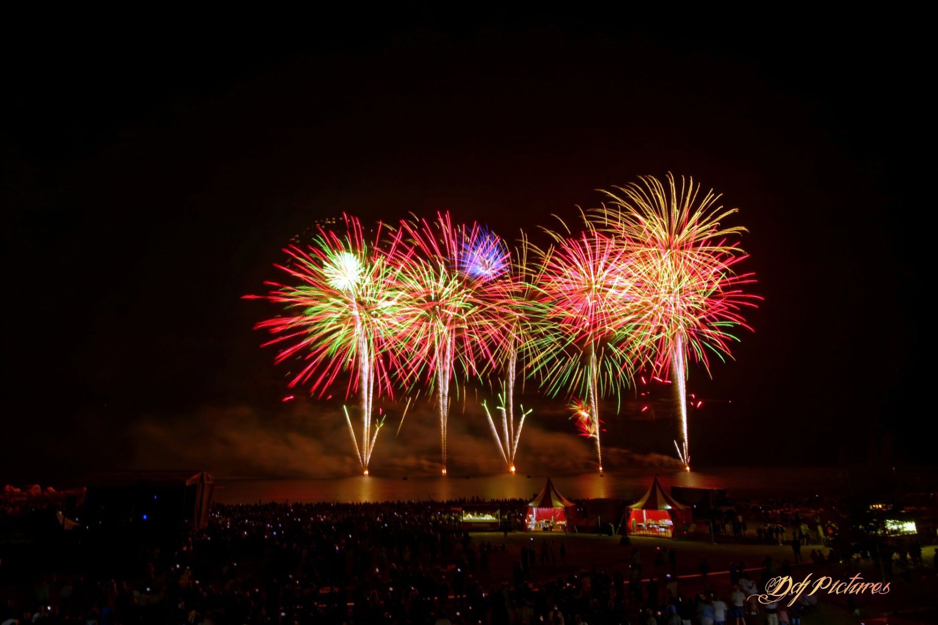 Effets pyrotechniques orange, violet et bleu avec gerbes basses sur les rives du lac de Madine en Meuse, spectacle musical tiré sur l'eau le 9 août 2025 par JSE société de Wagnon Group.