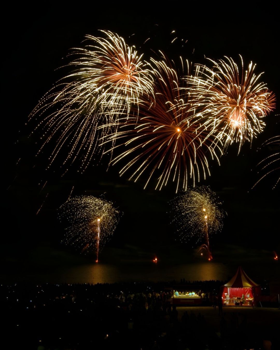 Gerbes de feux d'artifice dorées et orangées explosant au-dessus du lac de Madine devant une foule nombreuse, spectacle pyrotechnique sur mesure réalisé par Wagnon Group.