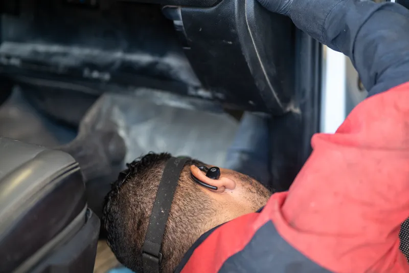 DOT inspection of a truck cab interior as a technician checks components beneath the dashboard.