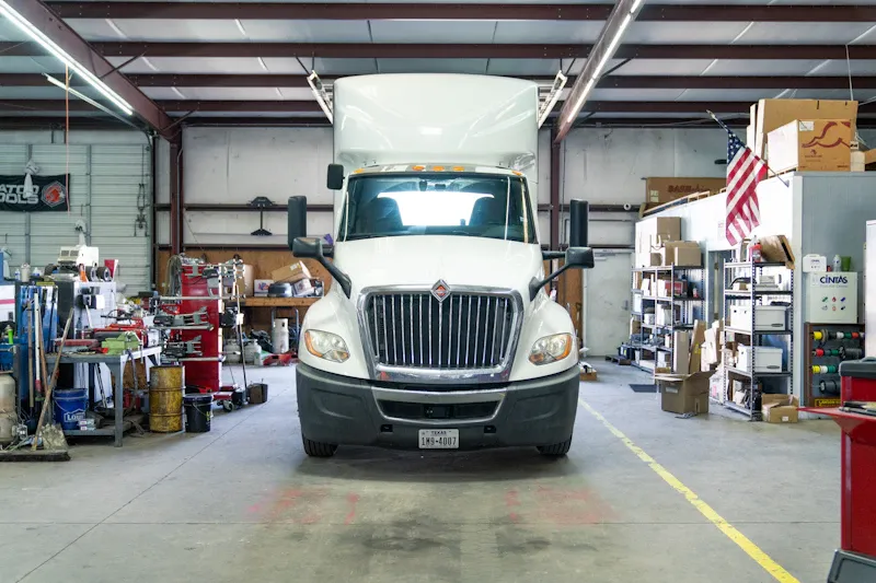 Heavy-duty repair on a box truck inside a service bay, ready for maintenance and fleet service. The truck displays a Texas license plate.
