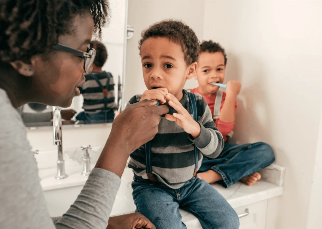 A woman brushing a child's teeth in a bathroom.