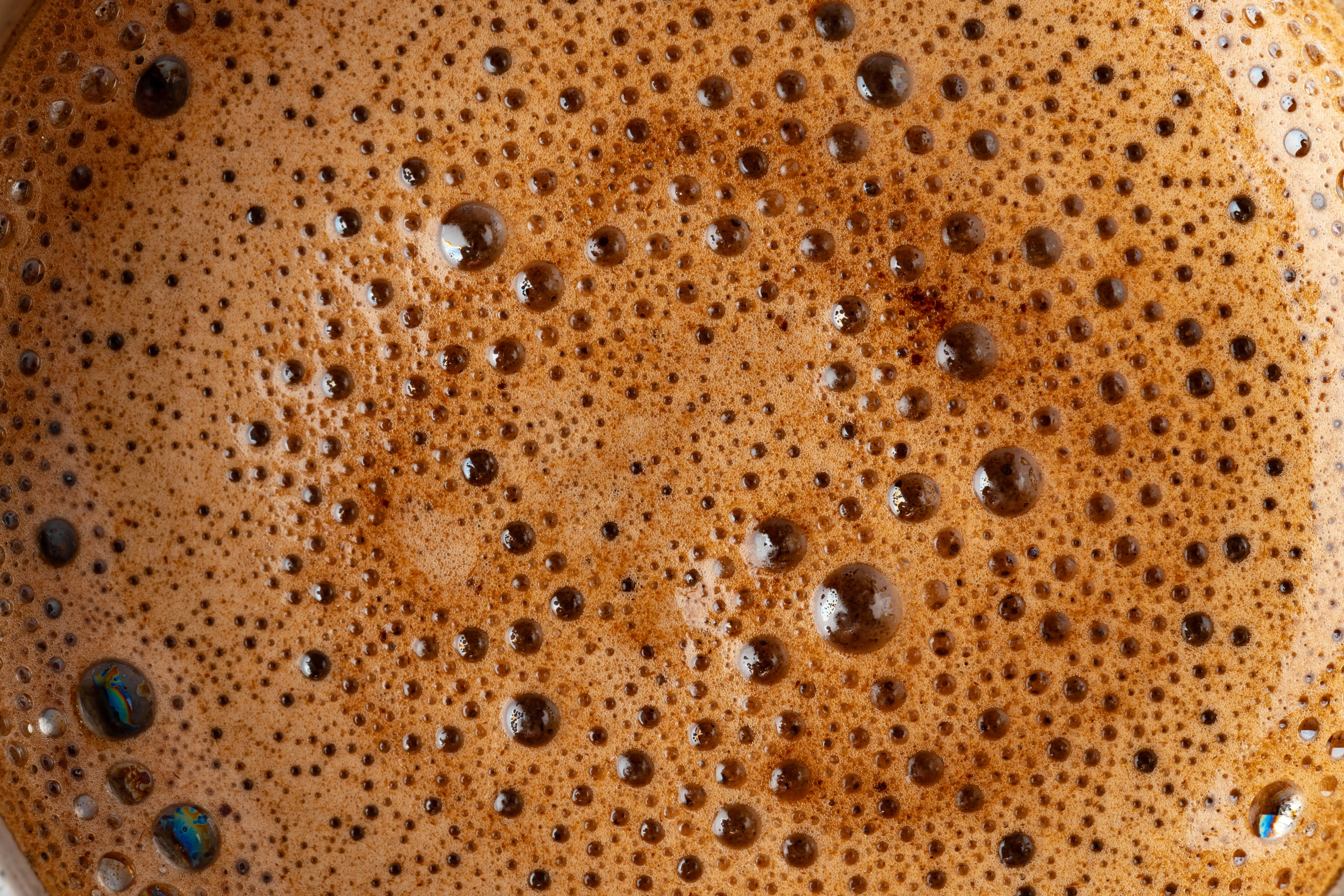 Close-up of brown coffee foam with small bubbles and smooth texture.