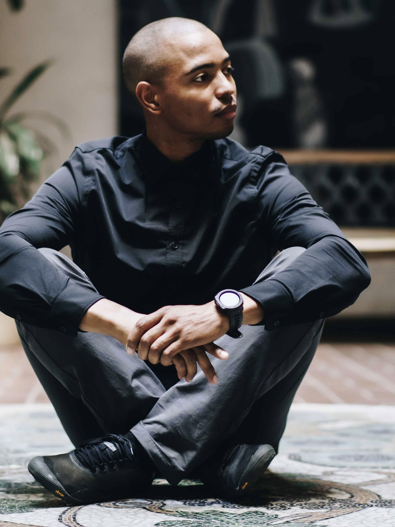 A person sits cross-legged indoors, looking off to the side.