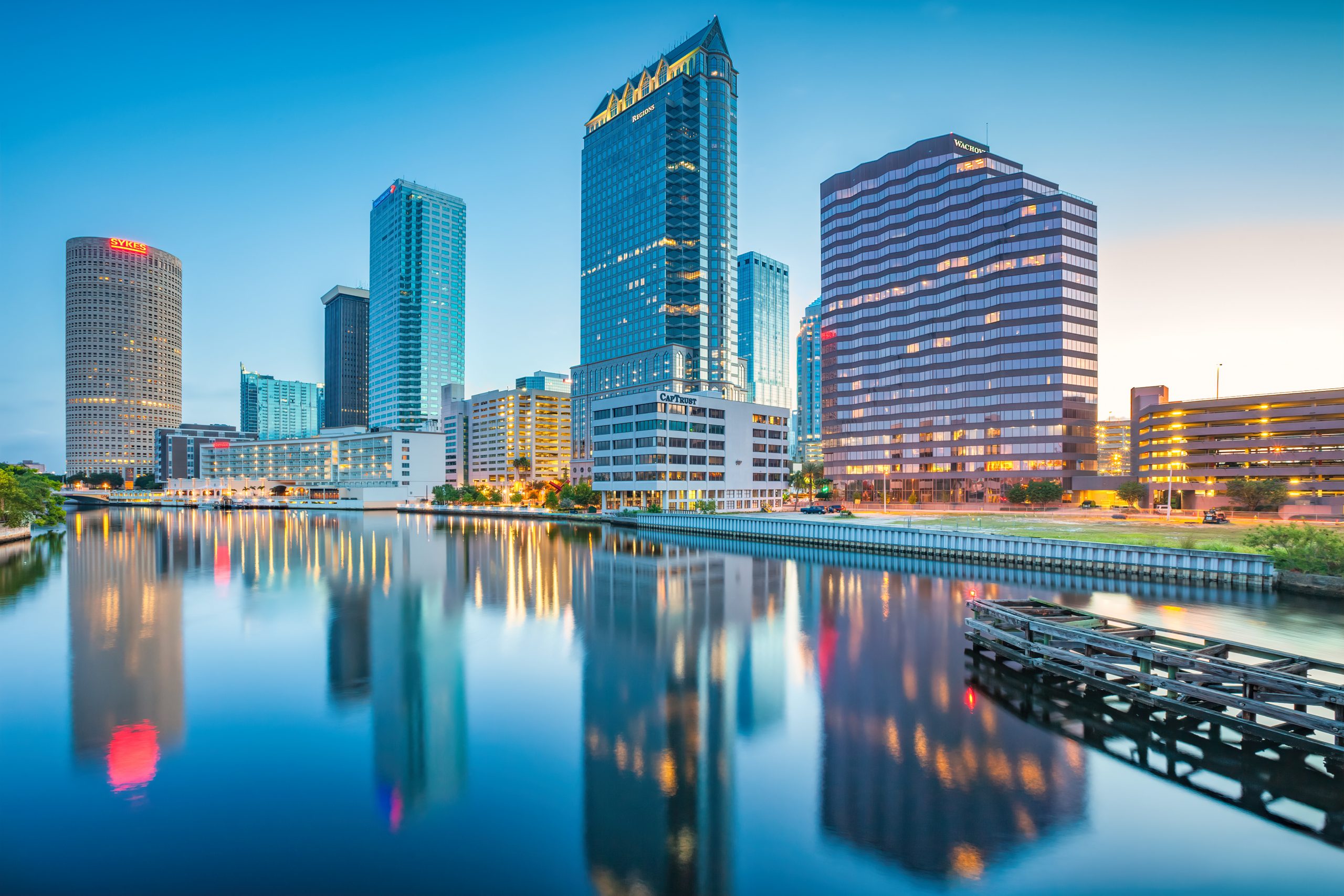 Marina with numerous boats docked, surrounded by high-rise buildings along a coastline under a blue sky with scattered clouds.