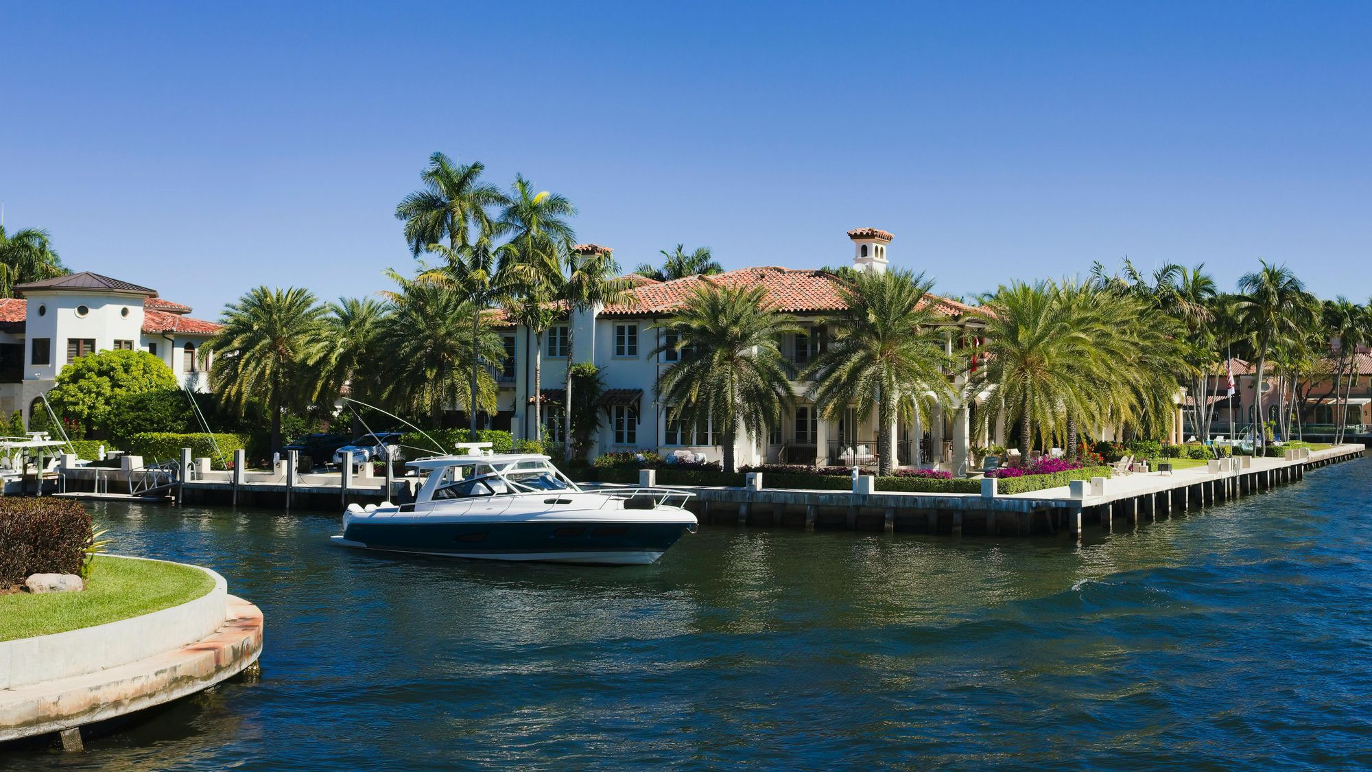 Marina with numerous boats docked, surrounded by high-rise buildings along a coastline under a blue sky with scattered clouds.