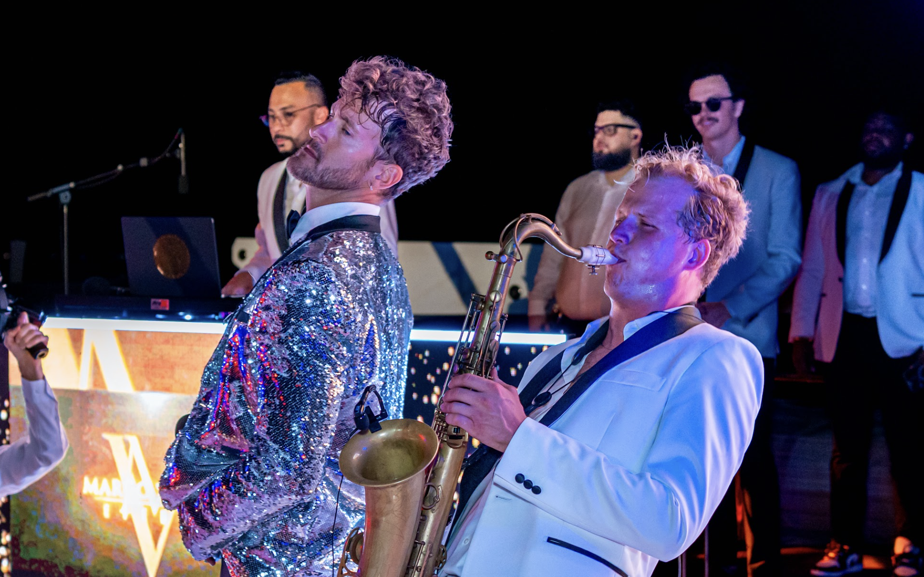 Saxophonist and performer in a sequined jacket on stage with the band