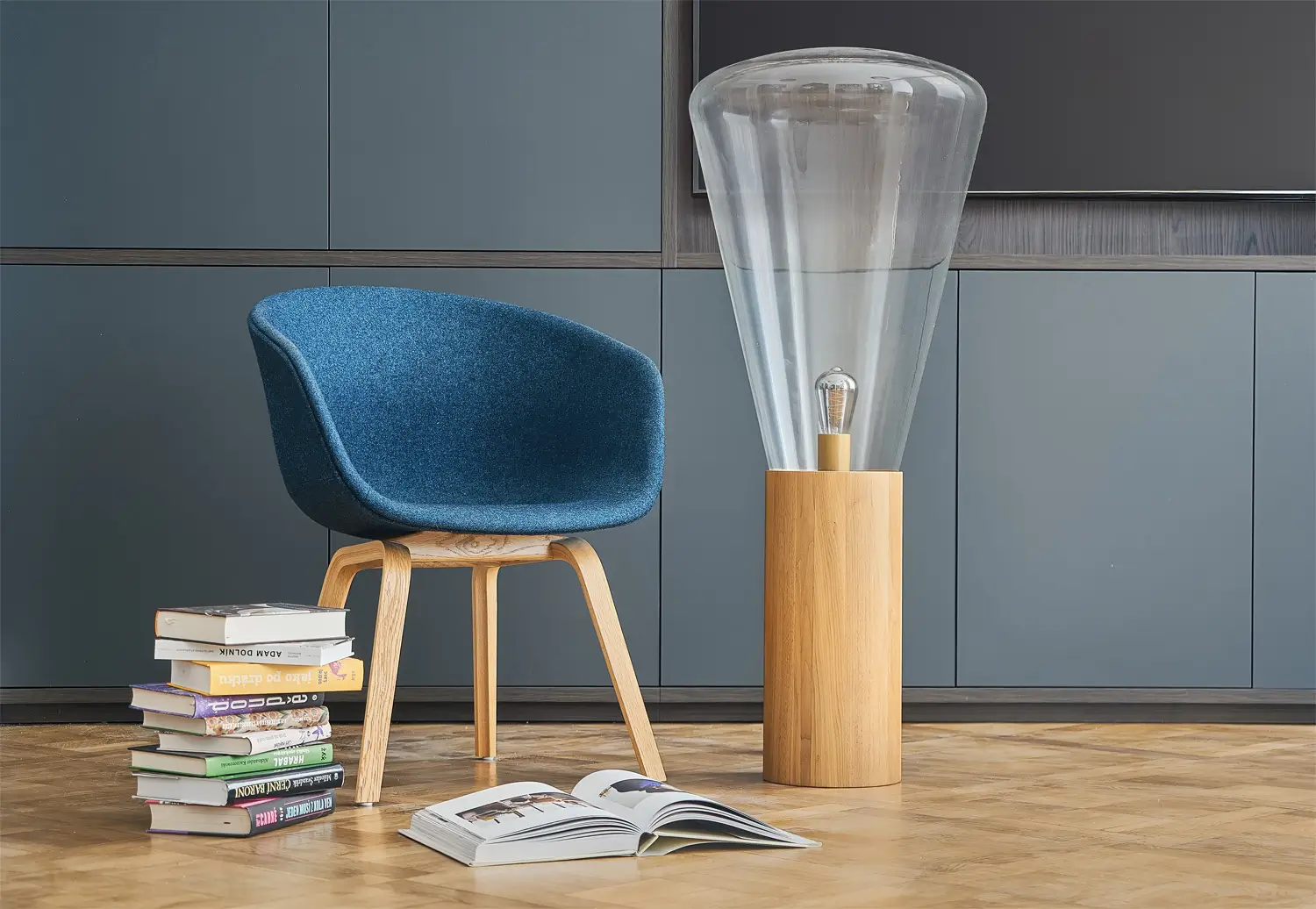 Zákoutí na čtení s modrým křeslem, skleněnou stojací lampou a knihami na parketové podlaze