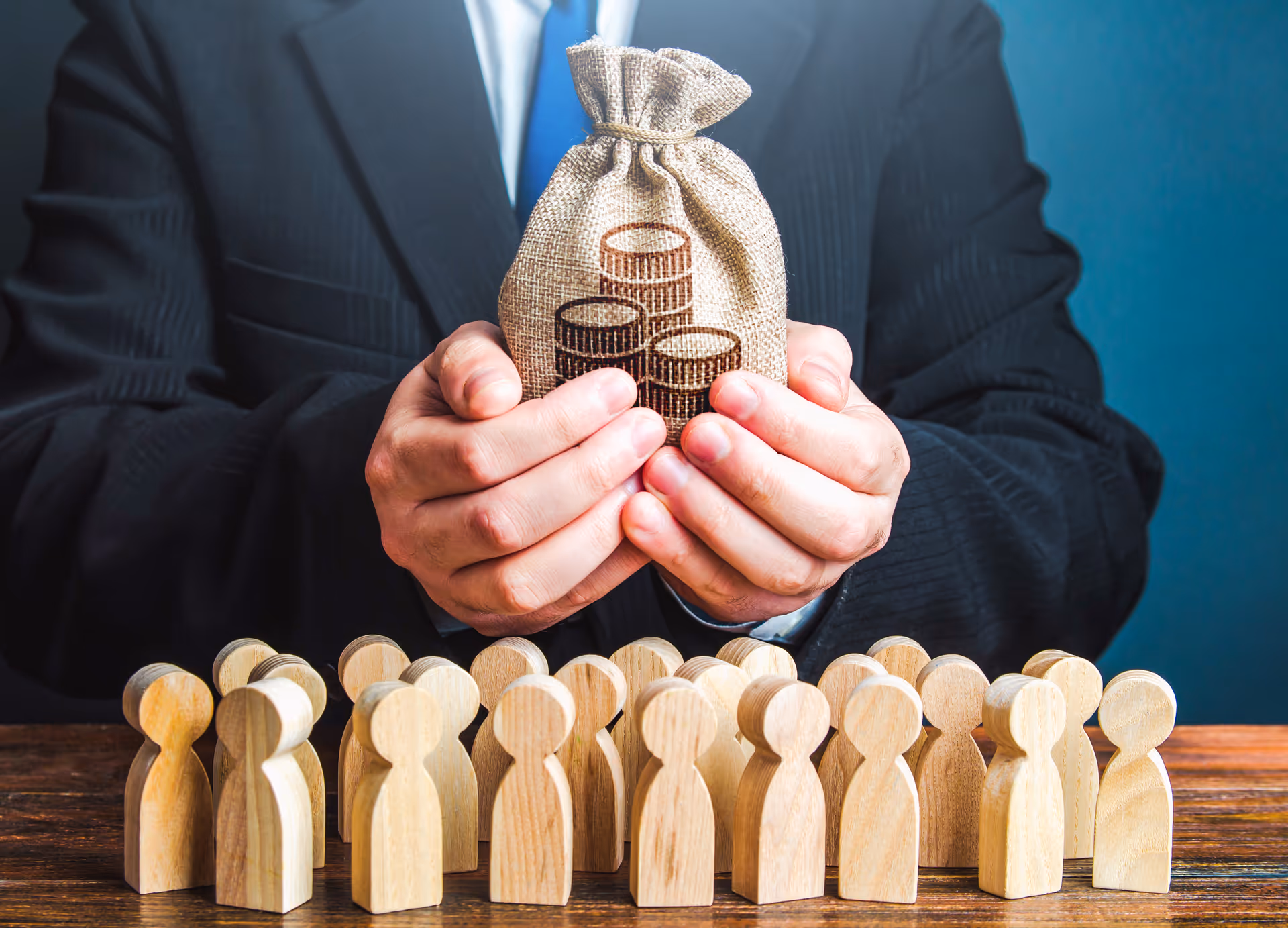 Businessperson holding a money bag above wooden figures, symbolizing budget allocation or compensation distribution