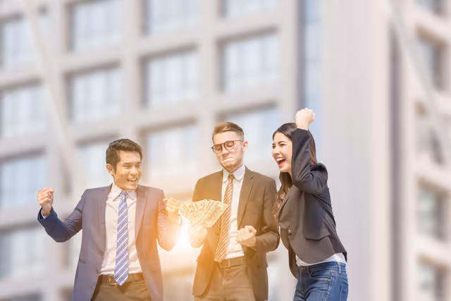 Three business professionals celebrating while holding cash outdoors