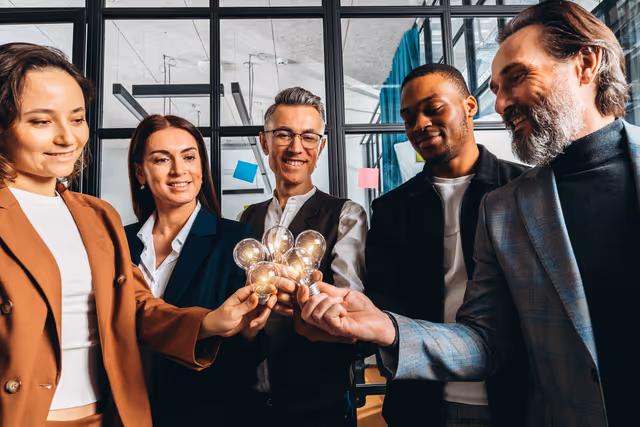 Diverse team holding glowing lightbulbs together, symbolizing shared ideas, innovation, and collaboration