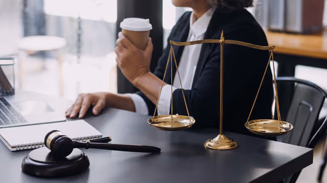 Desk with scales of justice and gavel beside a professional, symbolizing fairness, compliance, and transparent decisions