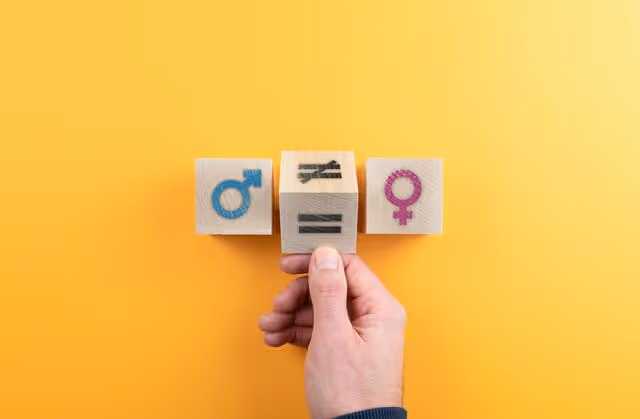 Hand holding wooden blocks with male, female, and equality symbols on a yellow background