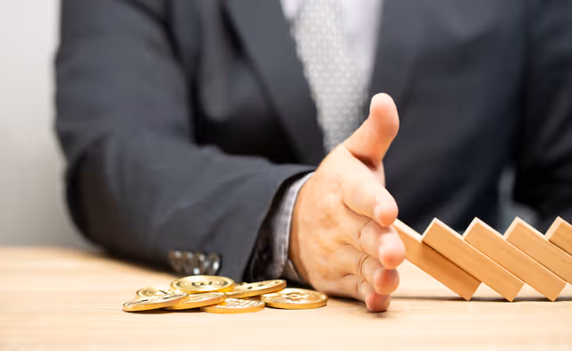 Businessperson stopping falling wooden blocks beside coins, symbolizing financial risk control