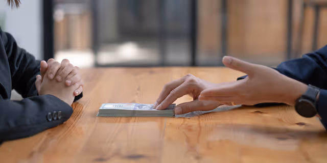 Two people in a discussion with money placed on the table, symbolizing negotiation or compensation