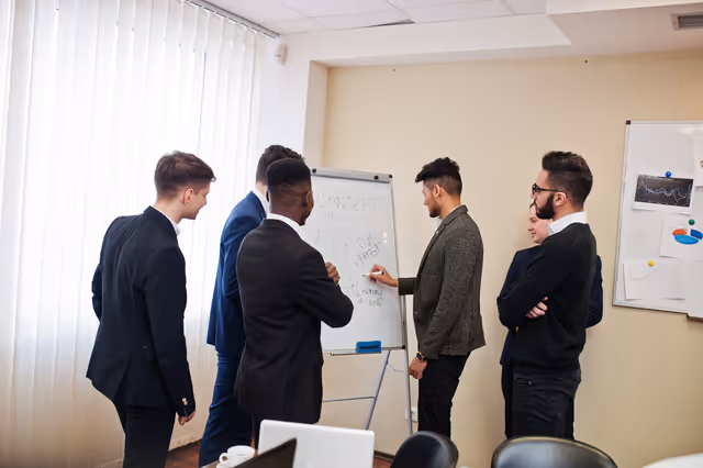 Employees collaborating around a whiteboard during a team meeting, discussing concepts and planning workplace strategies