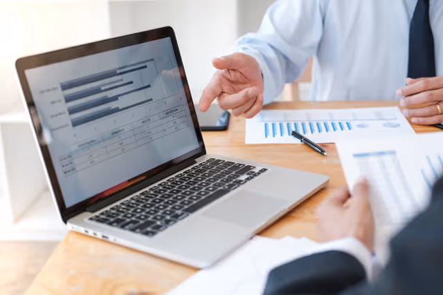Two professionals review charts on a laptop during a business discussion, analyzing data and performance metrics together