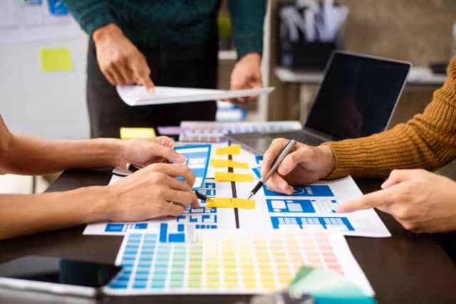 Team collaborating on design layouts with color palettes and wireframes spread across the table during a planning session