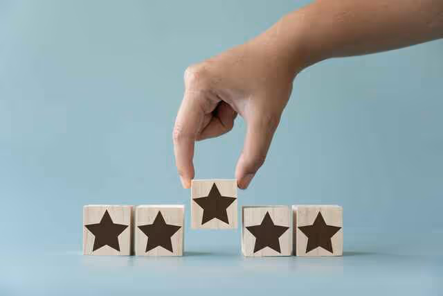 Hand placing a wooden star block among a row of rating blocks on a light blue background