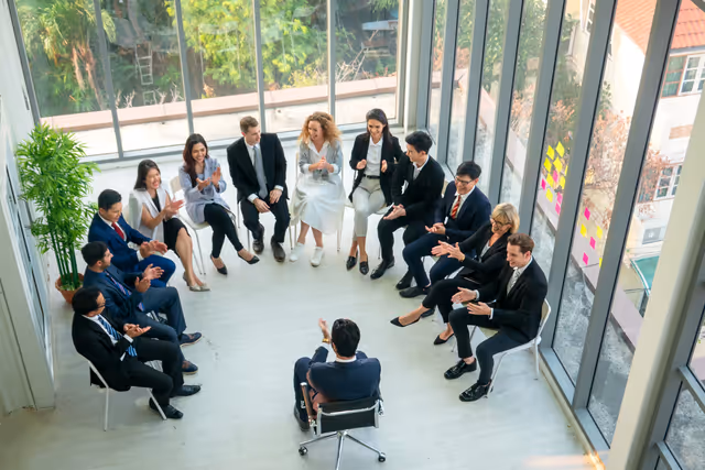 Business team seated in a circle during a meeting, engaging in discussion in a bright office space