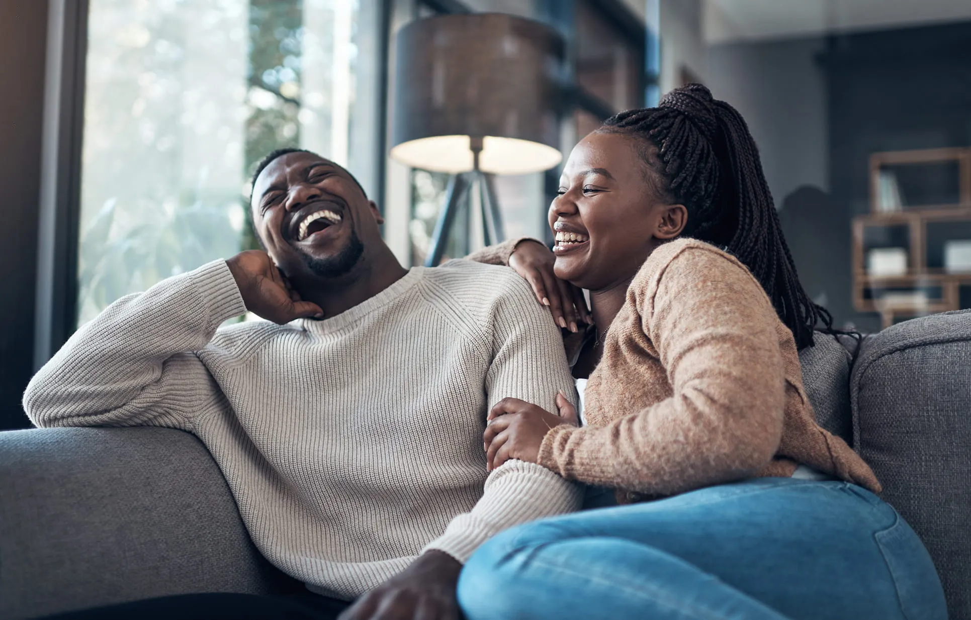 Couple sitting on a couch laughing together in a cozy living room.