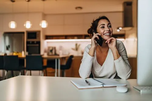 Smiling woman talking on phone while sitting at a table with an open notebook and pen.