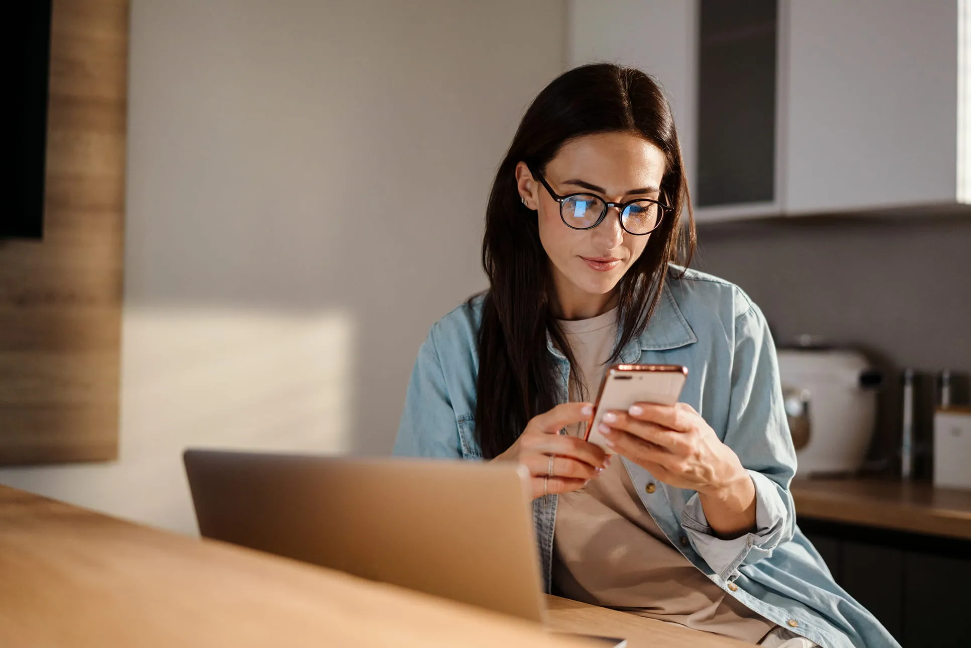 Woman looking at phone with laptop open in front of her