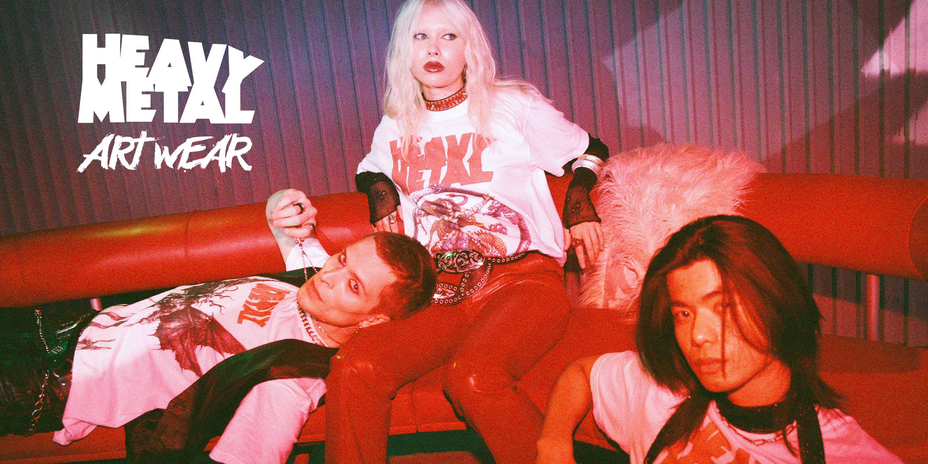 Three young adults in heavy metal art wear T-shirts posing on a red couch with moody lighting.