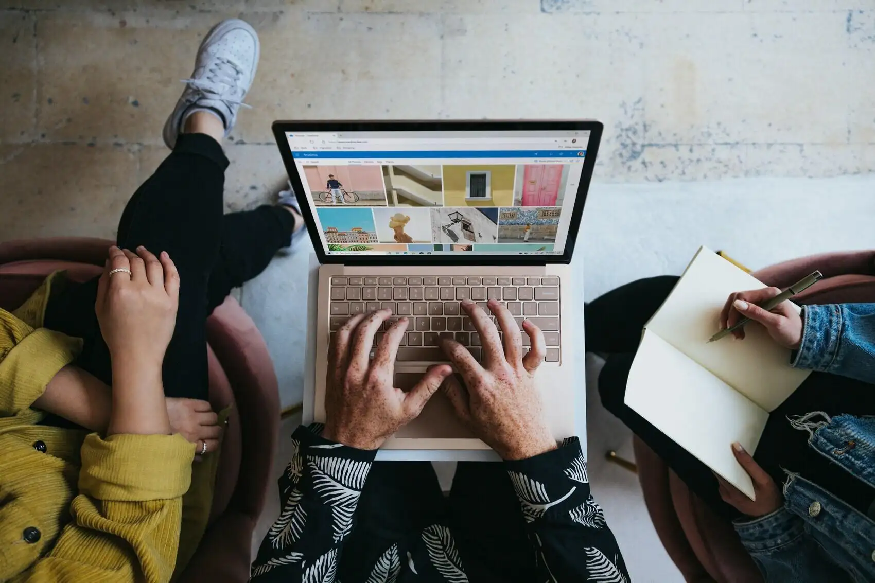 Three people sitting with one laptop on the lap and one person writing in notebook