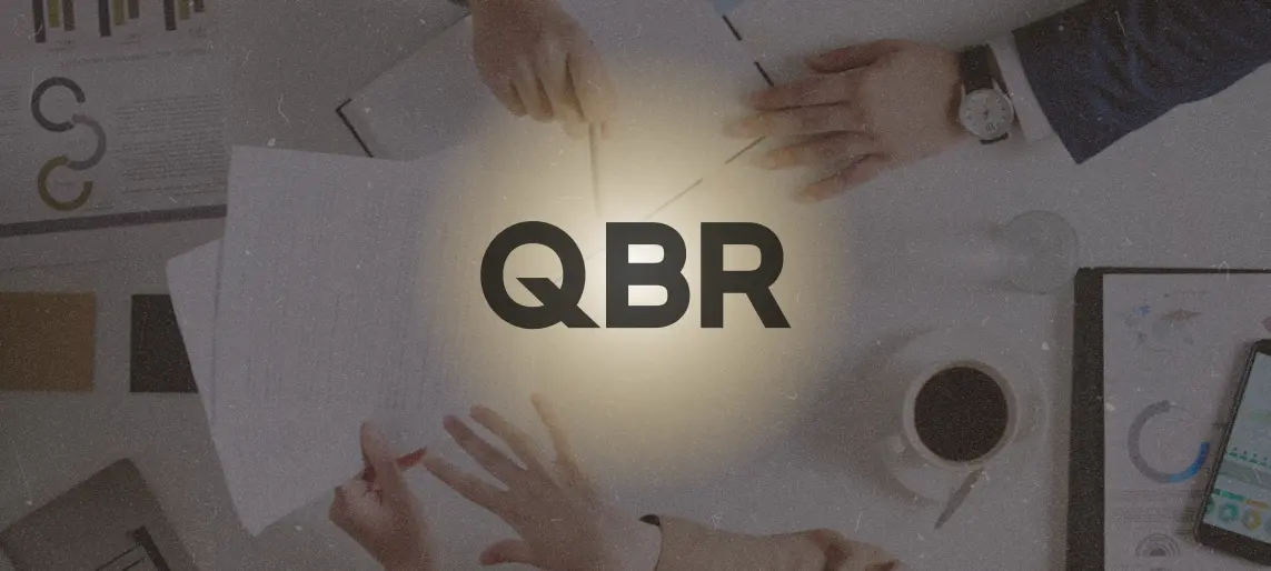 Team meeting around a table with documents and the letters QBR highlighted at the center.
