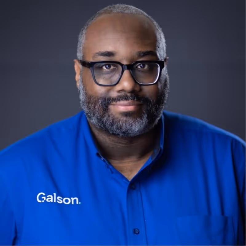 Middle-aged man with a beard and glasses wearing a blue Galson shirt against a dark gray background.