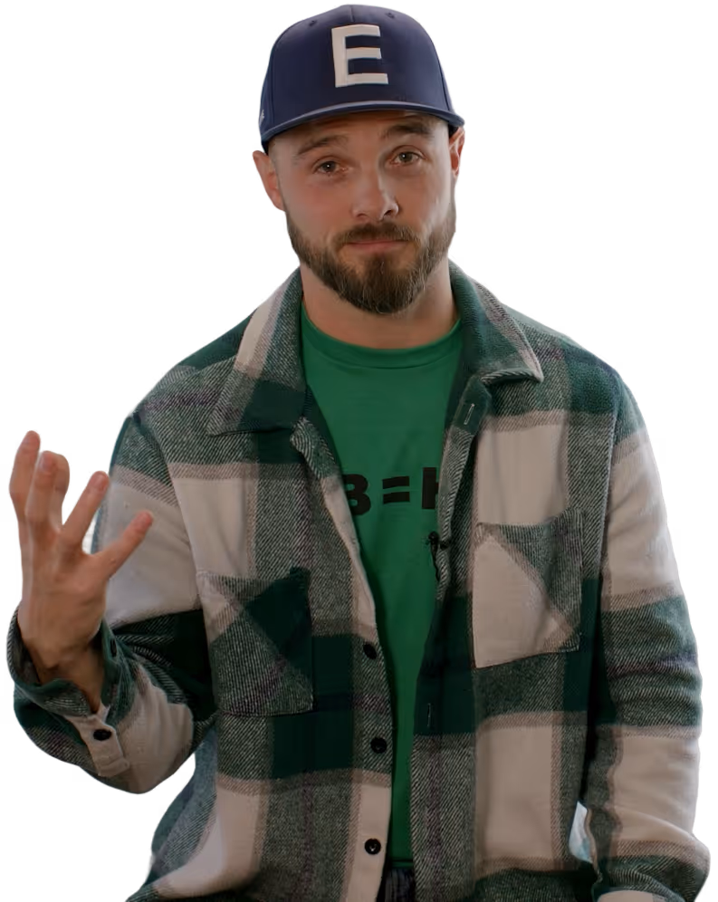 Bearded man wearing a blue cap with letter E, green shirt, and green plaid jacket, gesturing with one hand raised.