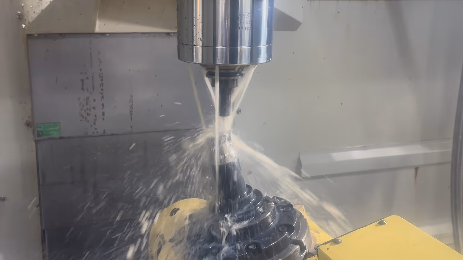 CNC machine milling a black metal gear while cutting fluid sprays to cool and lubricate the process.