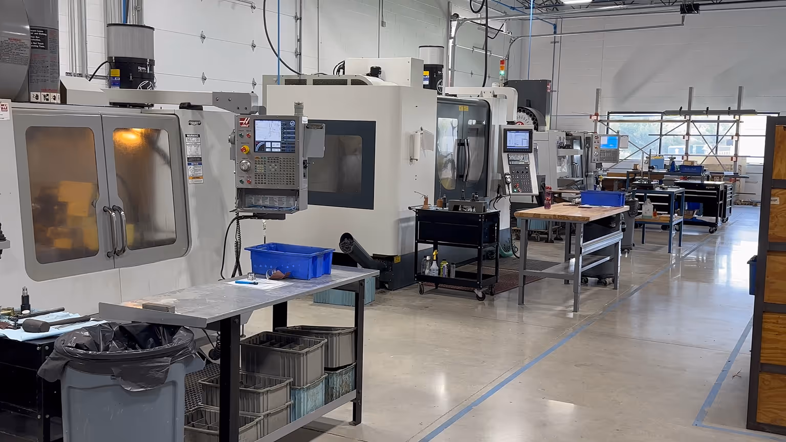 Modern industrial workshop with CNC machines, metal workbenches, and storage bins arranged in a clean, organized space.