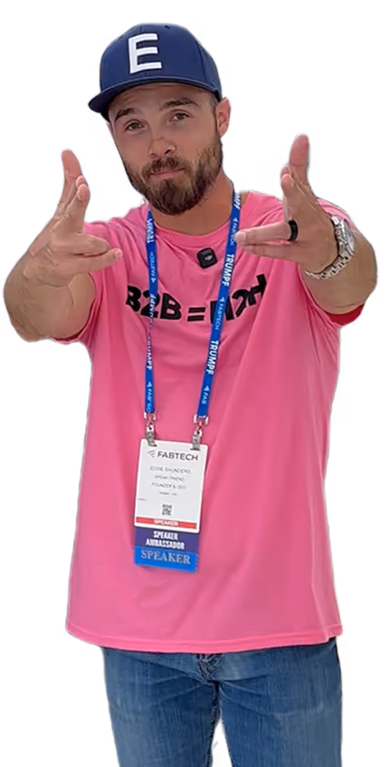 Eddie Saunders Jr. wearing a pink shirt, blue cap with letter E, and blue jeans pointing finger guns towards the camera with FABTECH speaker badge around his neck.