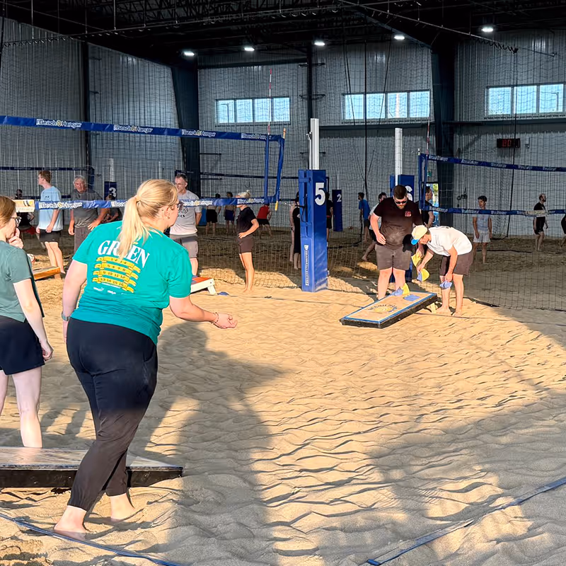 Group of people playing cornhole on a beach volleyball court at The Beach Hangar