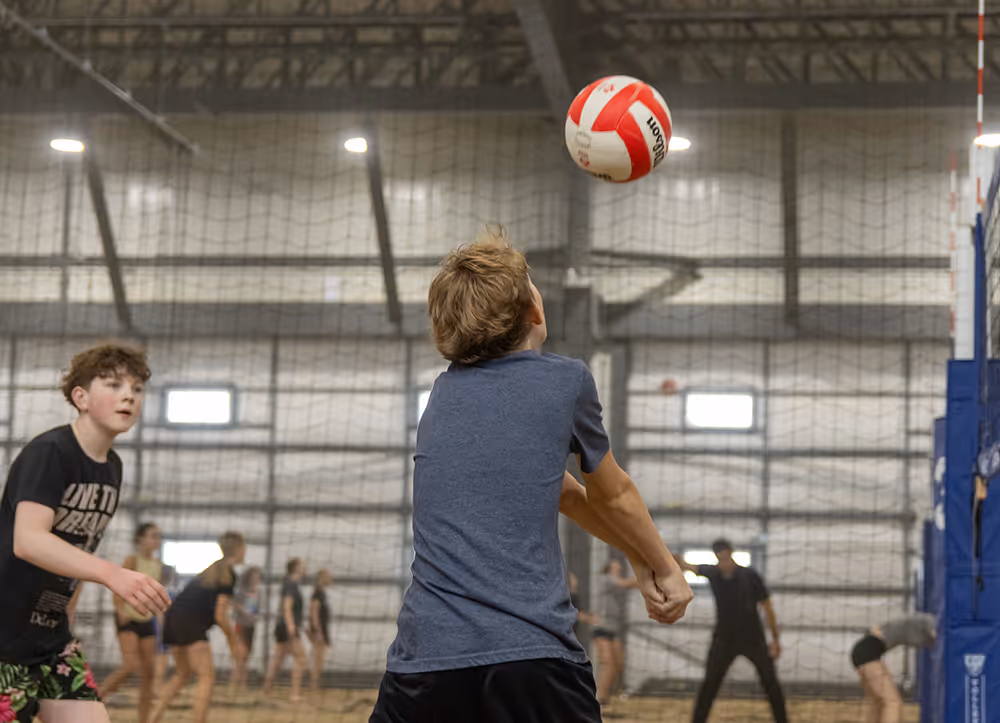 Young boys playing indoor volleyball with one preparing to bump the ball.