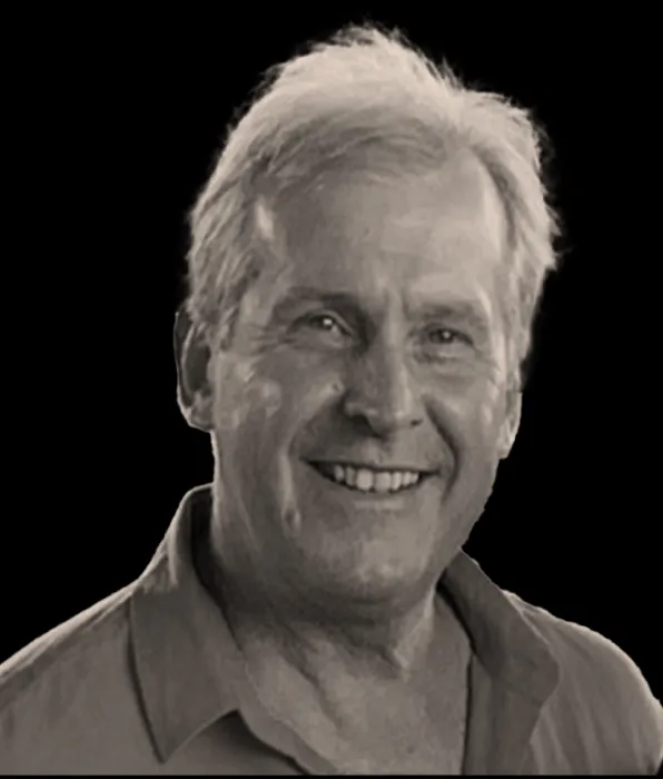 Smiling middle-aged man with light hair wearing a collared shirt against a black background.