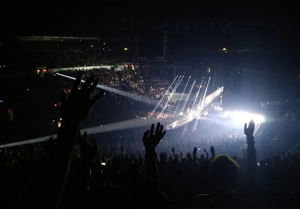 Crowd at a concert with raised hands and bright stage lights illuminating the performers.