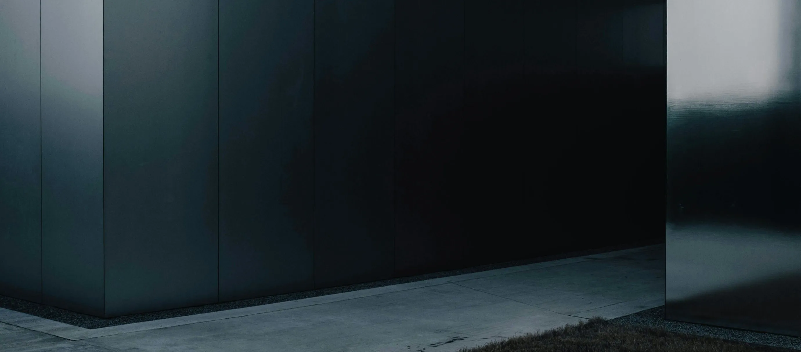 Modern building corner with dark, reflective metal panels and concrete pavement.