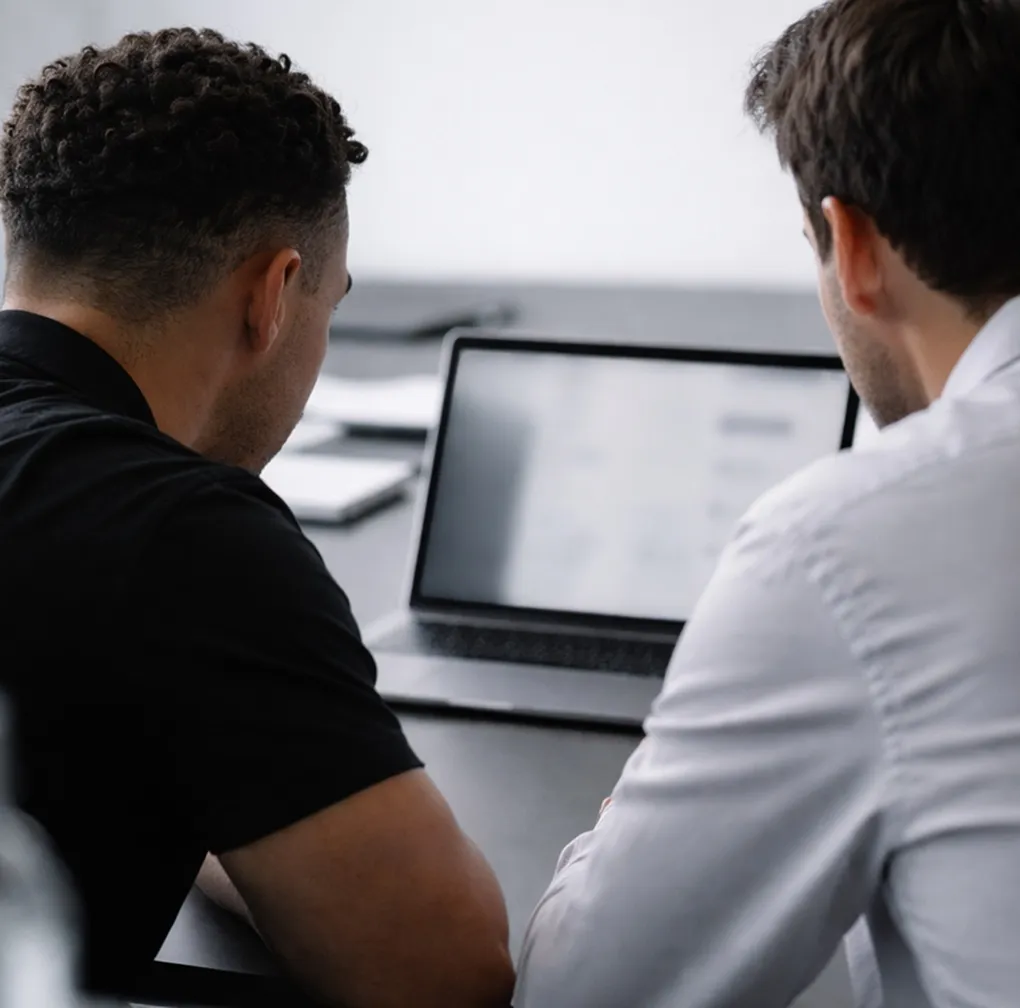 Four people seated around a conference table in a glass-walled office with large windows overlooking a cityscape.