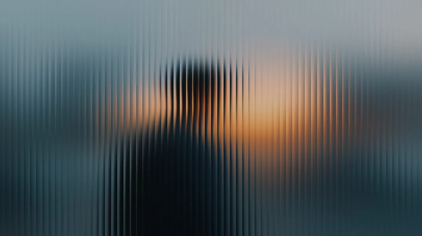 Man in a dark suit with a tie standing behind glass panels and concrete beams in an urban setting.