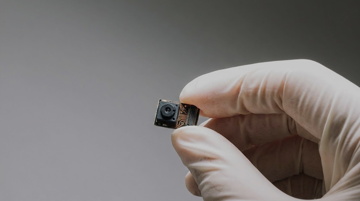 Man in a dark suit with a tie standing behind glass panels and concrete beams in an urban setting.