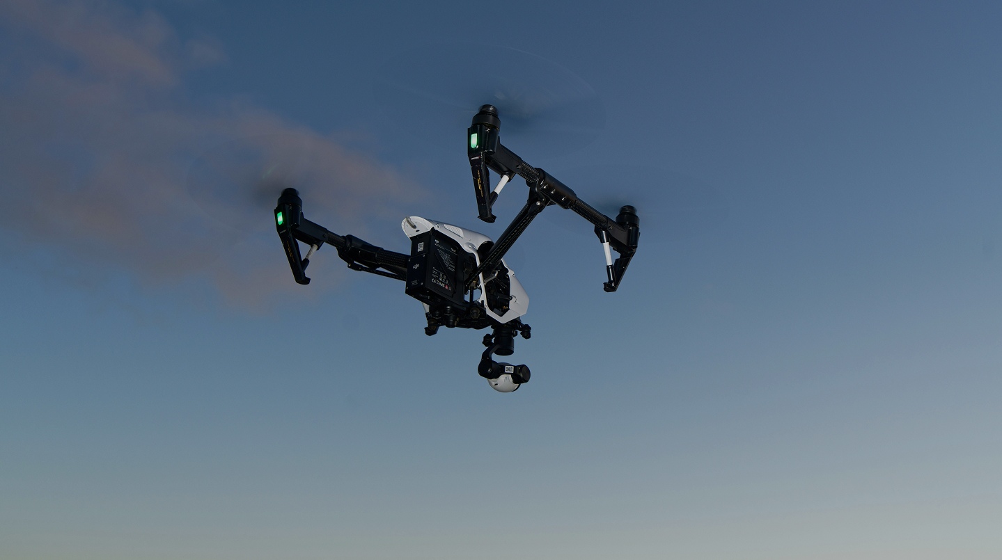 Man in a dark suit with a tie standing behind glass panels and concrete beams in an urban setting.