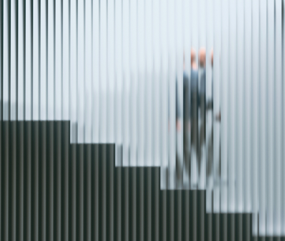 Blurred silhouette of a businessperson walking and talking on a phone beside a tiled urban building.