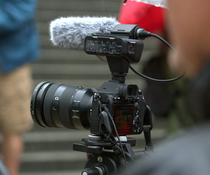 Four people seated around a conference table in a glass-walled office with large windows overlooking a cityscape.